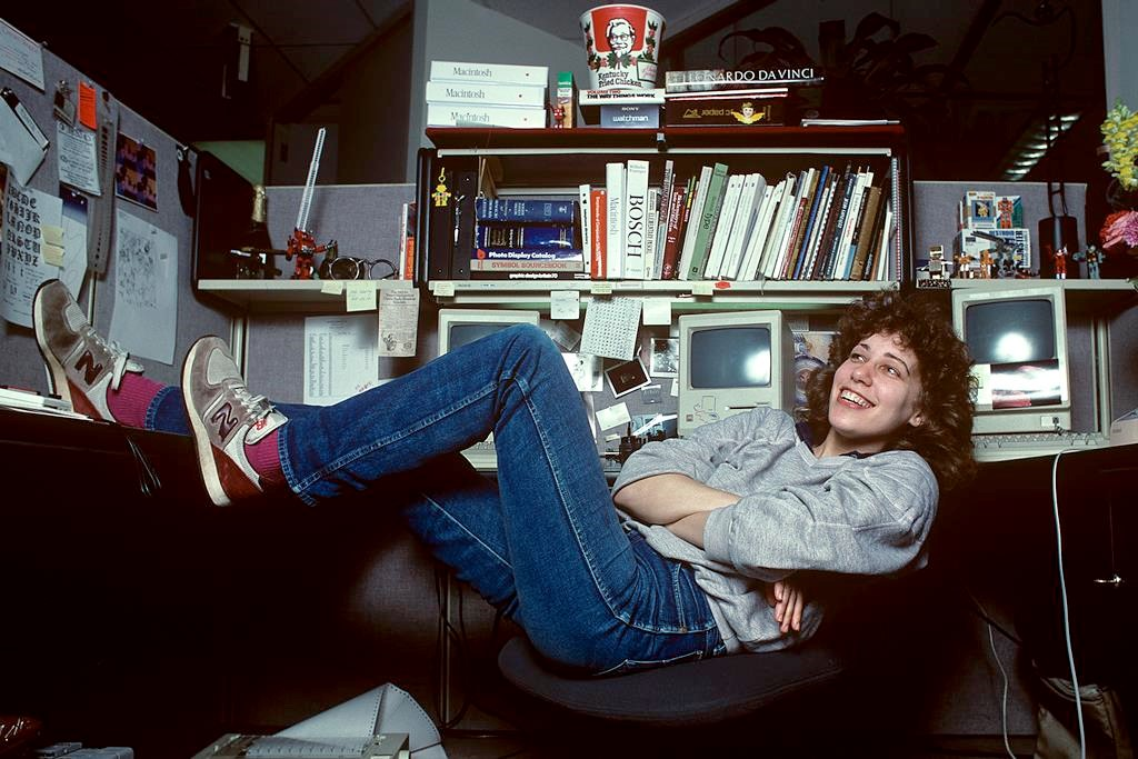 Susan Kare sitting at her cubicle smiling to the camera